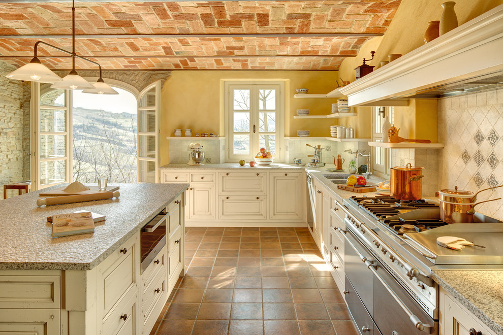This is an example of a large country l-shaped kitchen in Bologna with granite benchtops, stainless steel appliances, terra-cotta floors, with island, a double-bowl sink, beige cabinets, multi-coloured splashback and orange floor.