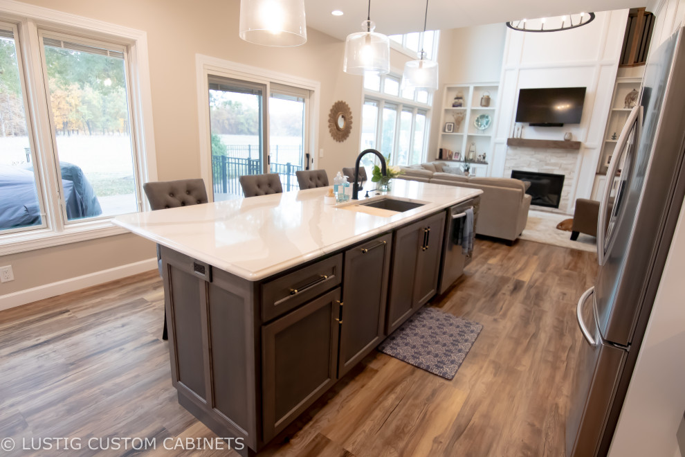 Example of a large transitional l-shaped laminate floor and brown floor open concept kitchen design with an undermount sink, flat-panel cabinets, white cabinets, quartz countertops, white backsplash, ceramic backsplash, stainless steel appliances, an island and white countertops