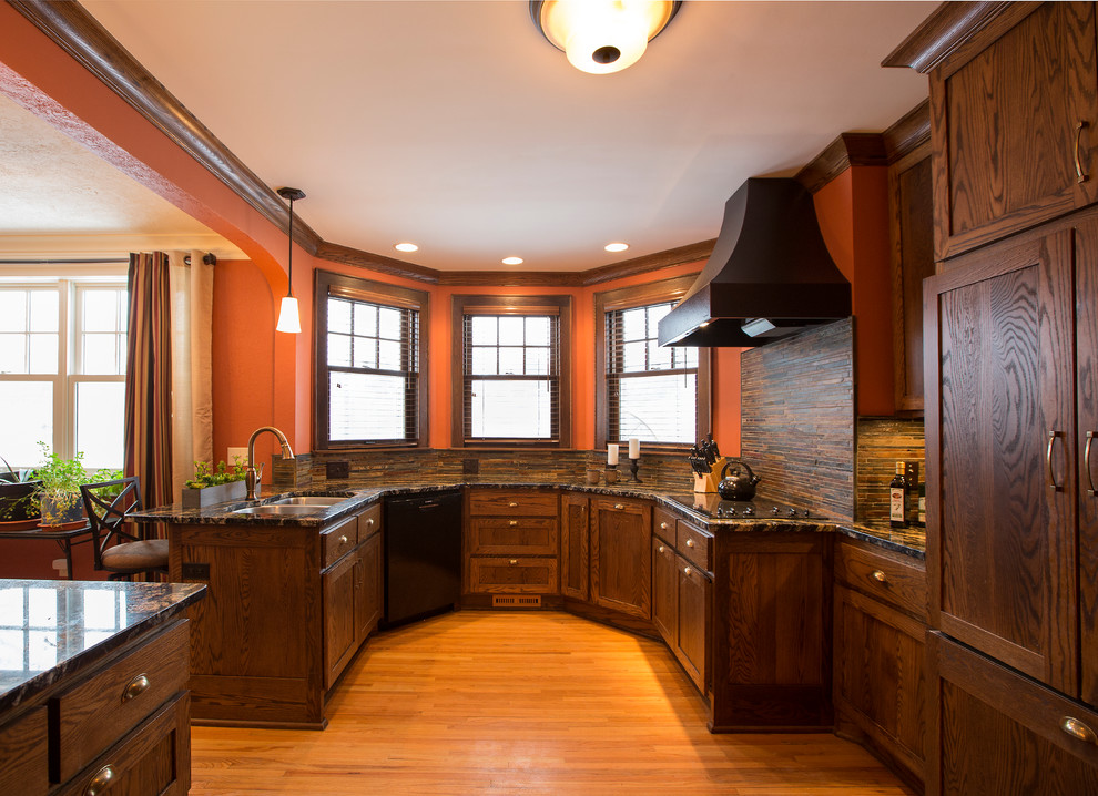 Inspiration for a traditional u-shaped kitchen in Minneapolis with an undermount sink, shaker cabinets, dark wood cabinets, granite benchtops, brown splashback, stone tile splashback, black appliances, light hardwood floors and a peninsula.