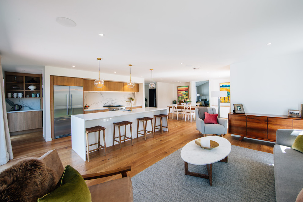 This is an example of a large kitchen pantry in Christchurch with an undermount sink, flat-panel cabinets, light wood cabinets, quartz benchtops, white splashback, porcelain splashback, stainless steel appliances, light hardwood floors, with island and brown floor.