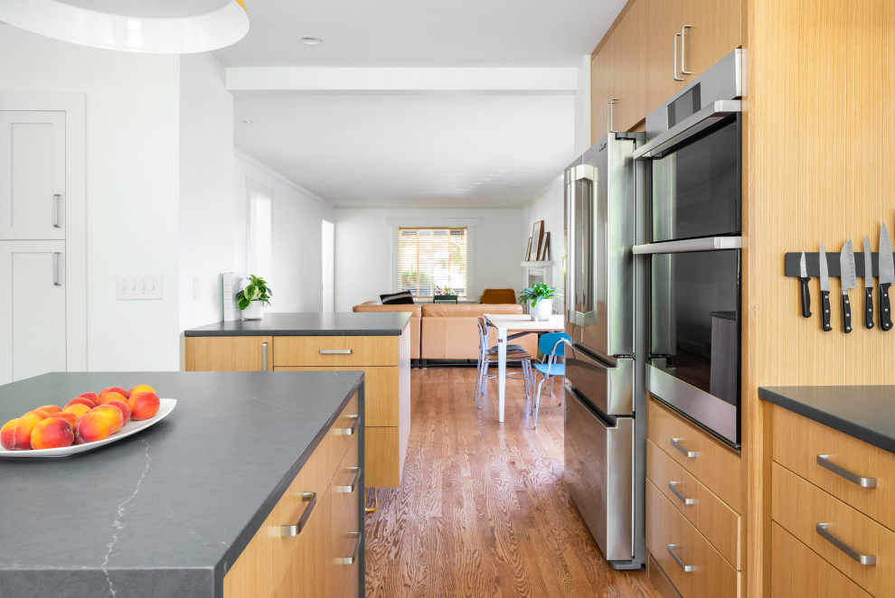 Photo of a mid-sized midcentury l-shaped separate kitchen in Seattle with flat-panel cabinets, medium wood cabinets, white splashback, stainless steel appliances, medium hardwood floors, with island, soapstone benchtops and black benchtop.