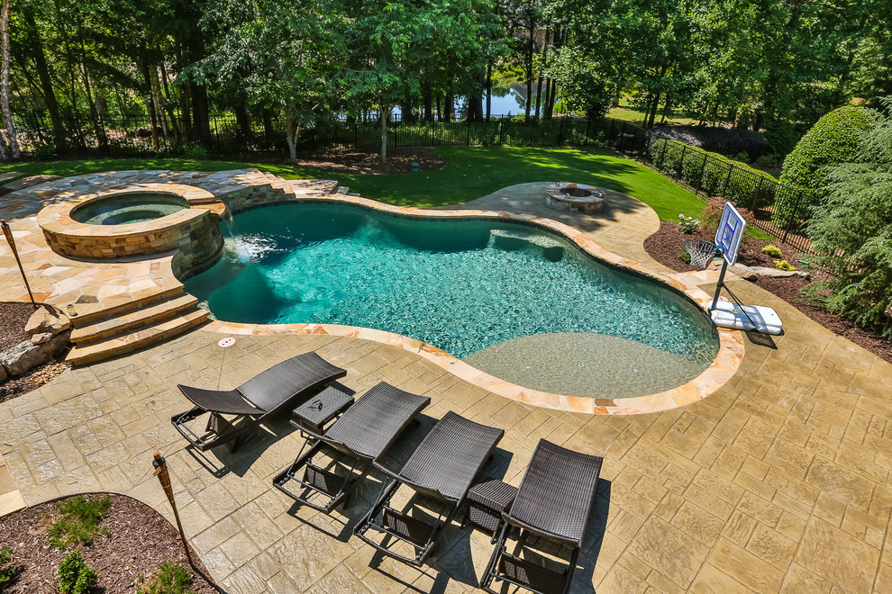 Inspiration for a large tropical backyard custom-shaped natural pool in Atlanta with a water feature and stamped concrete.