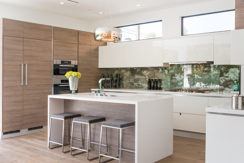 This is an example of a mid-sized contemporary l-shaped kitchen in Los Angeles with an undermount sink, flat-panel cabinets, white cabinets, multi-coloured splashback, stainless steel appliances, light hardwood floors and with island.