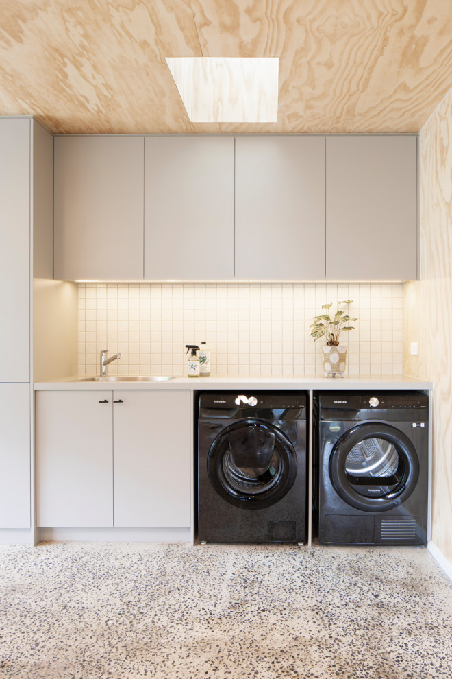 Example of a small trendy single-wall concrete floor, wood ceiling and wood wall utility room design in Melbourne with a single-bowl sink, flat-panel cabinets, beige cabinets, laminate countertops, white backsplash, mosaic tile backsplash, beige walls, a side-by-side washer/dryer and beige countertops