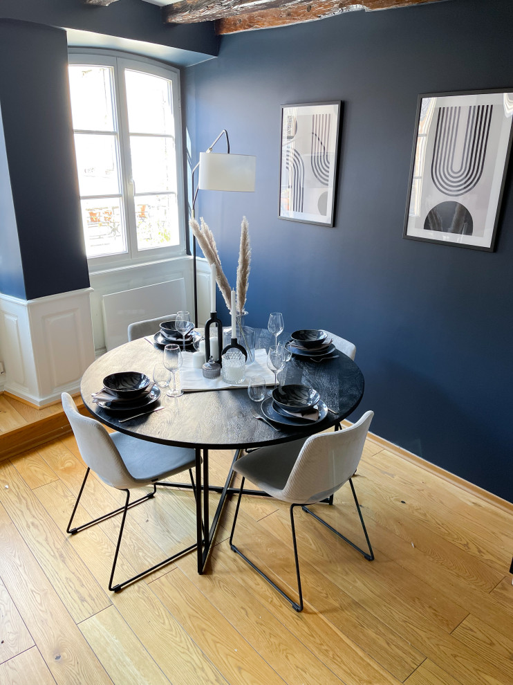 Cette image montre une salle à manger ouverte sur le salon traditionnelle de taille moyenne avec un mur bleu, parquet clair, aucune cheminée, un sol jaune, poutres apparentes et éclairage.