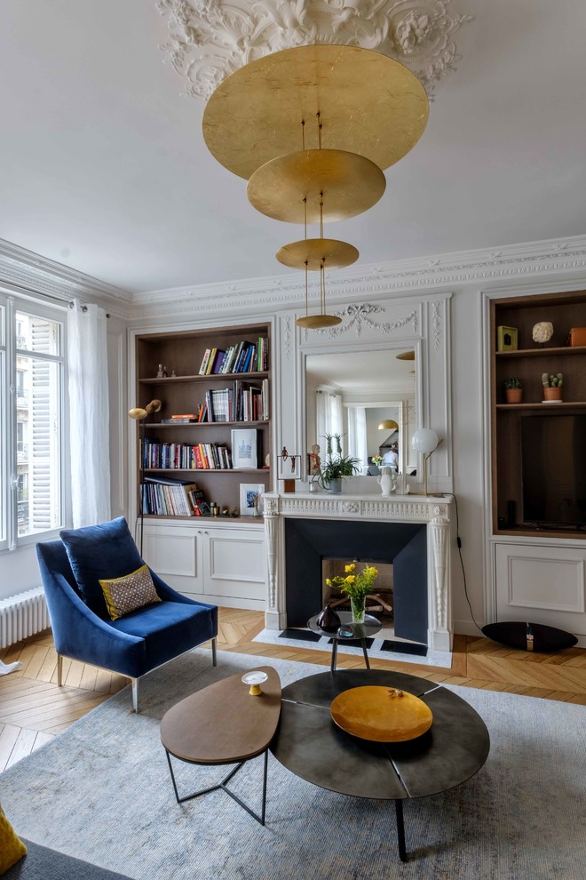 Design ideas for a large traditional enclosed living room in Paris with a library, white walls, light hardwood floors, a standard fireplace, a plaster fireplace surround, a built-in media wall and brown floor.