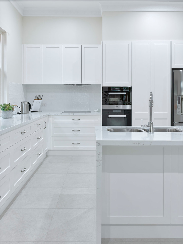 Photo of a large contemporary l-shaped open plan kitchen in Other with a double-bowl sink, shaker cabinets, white cabinets, quartz benchtops, white splashback, ceramic splashback, stainless steel appliances, porcelain floors, with island and white benchtop.