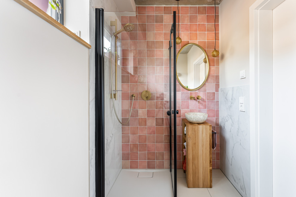 This is an example of a small modern powder room in Frankfurt with open cabinets, medium wood cabinets, a wall-mount toilet, pink tile, ceramic tile, beige walls, ceramic floors, a vessel sink, wood benchtops, beige floor, brown benchtops and a freestanding vanity.