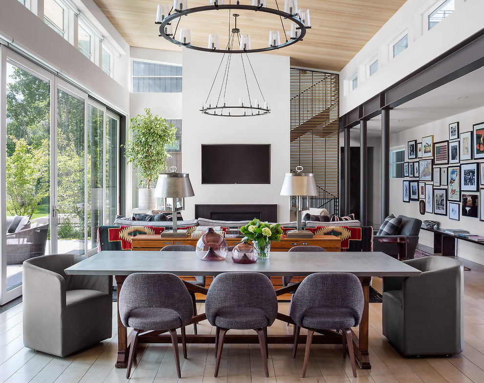 Large contemporary dining room in Denver with white walls, light hardwood floors, a standard fireplace, a metal fireplace surround and brown floor.