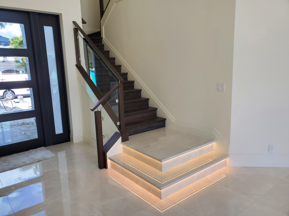 Large modern tile u-shaped staircase in Miami with tile risers and glass railing.