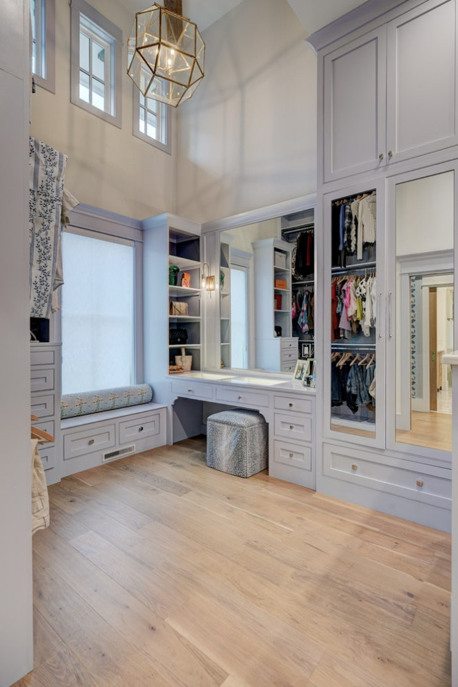 Modelo de armario vestidor clásico grande con armarios con rebordes decorativos, puertas de armario azules, suelo de madera clara y vigas vistas