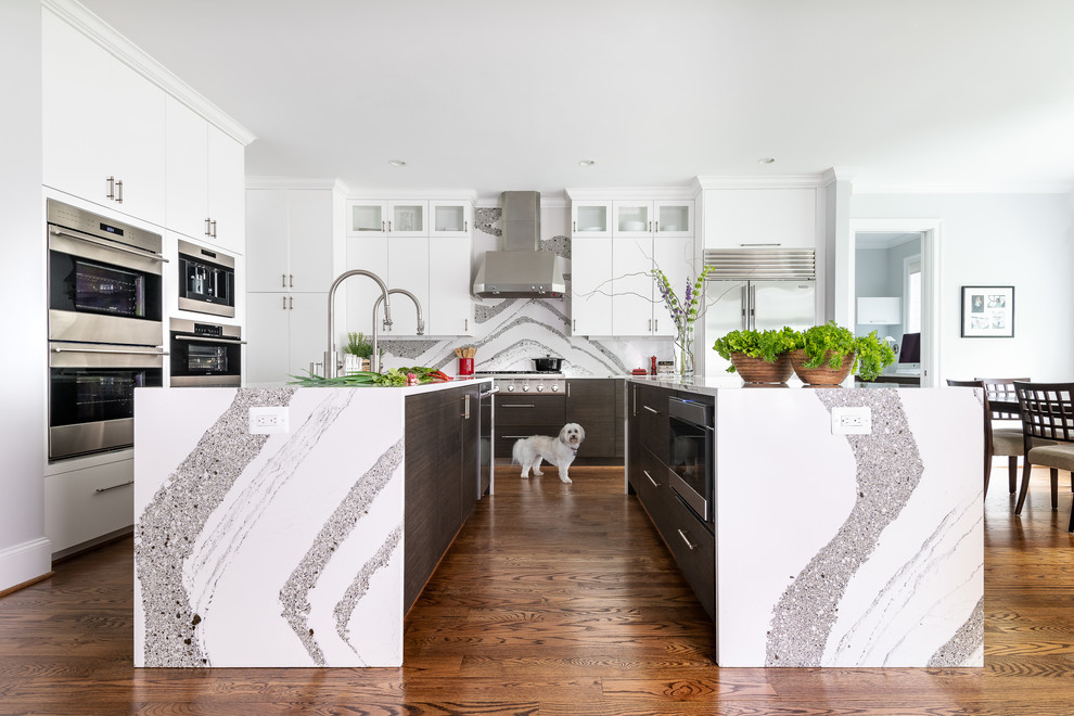 Design ideas for a large contemporary open plan kitchen in DC Metro with flat-panel cabinets, white cabinets, stainless steel appliances, medium hardwood floors, multiple islands, white benchtop, multi-coloured splashback and stone slab splashback.