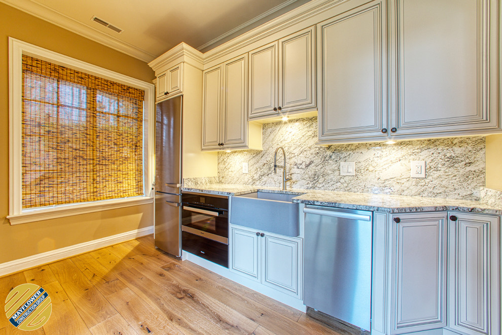 Photo of a small transitional single-wall eat-in kitchen in DC Metro with a farmhouse sink, raised-panel cabinets, beige cabinets, granite benchtops, grey splashback, granite splashback, stainless steel appliances, light hardwood floors, no island, beige floor and grey benchtop.