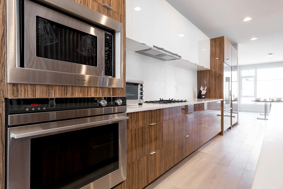 Mid-sized contemporary single-wall eat-in kitchen in Edmonton with an undermount sink, flat-panel cabinets, granite benchtops, white splashback, stainless steel appliances, light hardwood floors and with island.
