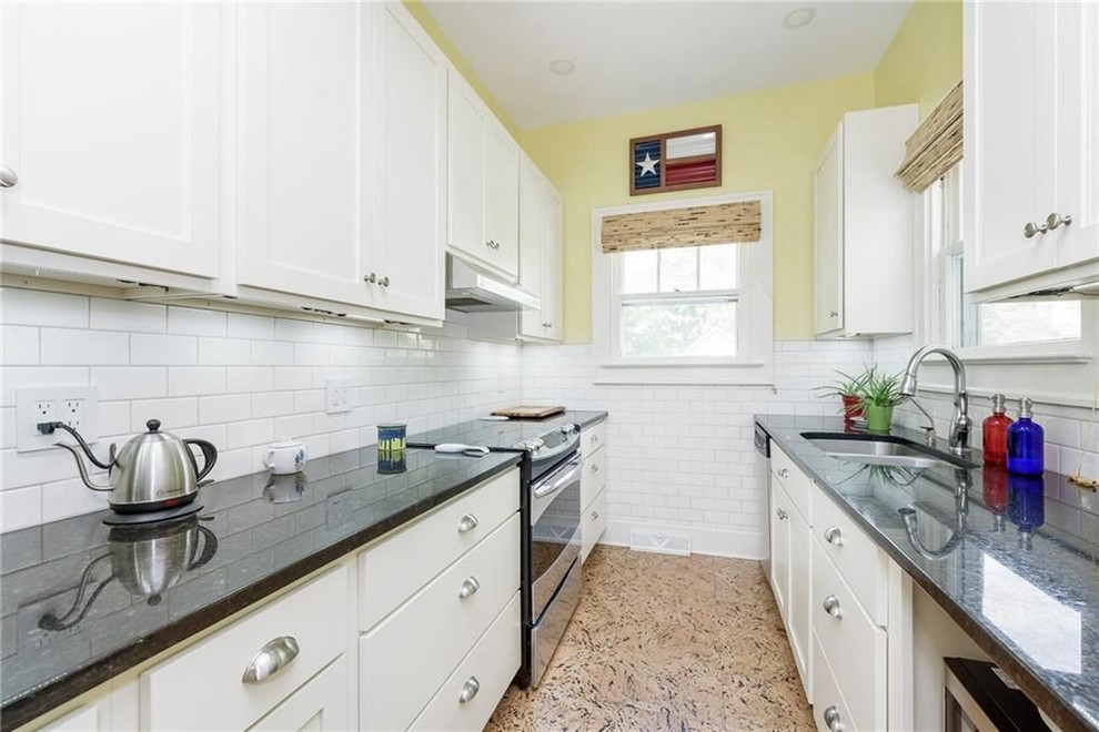 This is an example of a mid-sized arts and crafts galley separate kitchen in Indianapolis with recessed-panel cabinets, white cabinets, quartz benchtops, black splashback, subway tile splashback, stainless steel appliances, cork floors, no island, brown floor and black benchtop.