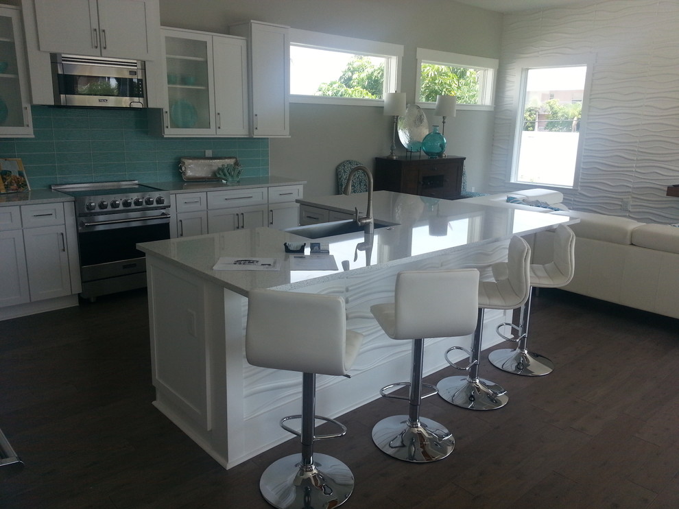 This is an example of a large beach style l-shaped eat-in kitchen in Tampa with a farmhouse sink, shaker cabinets, white cabinets, quartzite benchtops, green splashback, glass tile splashback, stainless steel appliances, medium hardwood floors and with island.