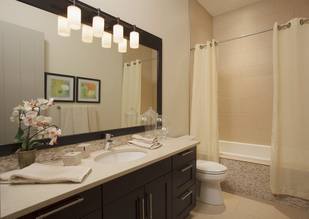Photo of a mid-sized contemporary 3/4 bathroom in Calgary with shaker cabinets, dark wood cabinets, an alcove tub, a shower/bathtub combo, a two-piece toilet, beige tile, glass tile, beige walls, porcelain floors, an undermount sink, solid surface benchtops, beige floor, a shower curtain and beige benchtops.