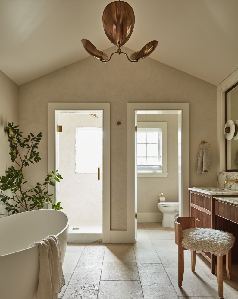 Photo of a transitional bathroom in San Francisco with flat-panel cabinets, medium wood cabinets, a freestanding tub, an alcove shower, beige walls, an undermount sink, beige floor, a hinged shower door, white benchtops, an enclosed toilet, a built-in vanity and vaulted.