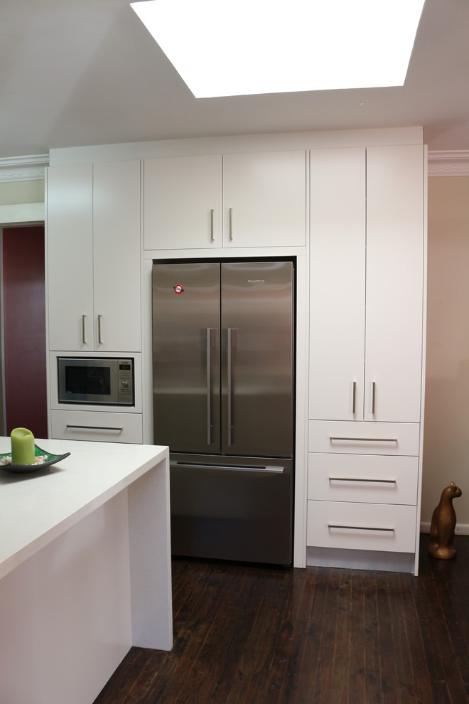 Large modern l-shaped open plan kitchen in Sydney with an undermount sink, flat-panel cabinets, white cabinets, quartz benchtops, brown splashback, glass sheet splashback, stainless steel appliances, multiple islands and white benchtop.