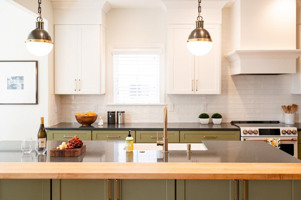 Photo of a large eclectic l-shaped eat-in kitchen in Denver with a farmhouse sink, shaker cabinets, green cabinets, wood benchtops, white splashback, ceramic splashback, white appliances, light hardwood floors, with island and black benchtop.