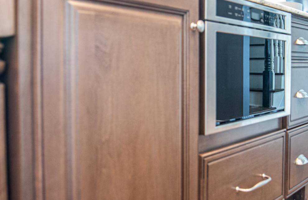 Example of a large transitional l-shaped medium tone wood floor and brown floor open concept kitchen design in Charlotte with a farmhouse sink, white cabinets, granite countertops, white backsplash, stainless steel appliances, an island, raised-panel cabinets, porcelain backsplash and white countertops