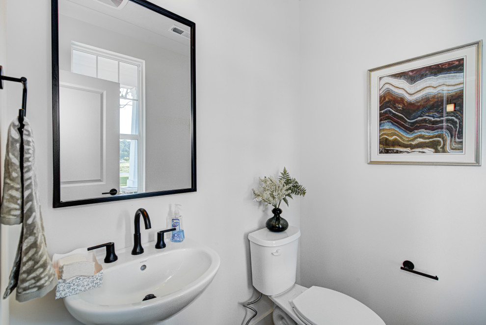 Bild på ett mellanstort amerikanskt toalett, med en toalettstol med hel cisternkåpa, vita väggar, vinylgolv, ett piedestal handfat och brunt golv