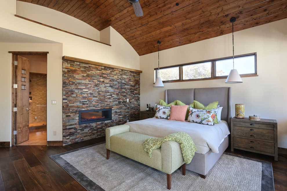 Photo of a country bedroom in Denver with white walls, dark hardwood floors, a two-sided fireplace and a stone fireplace surround.