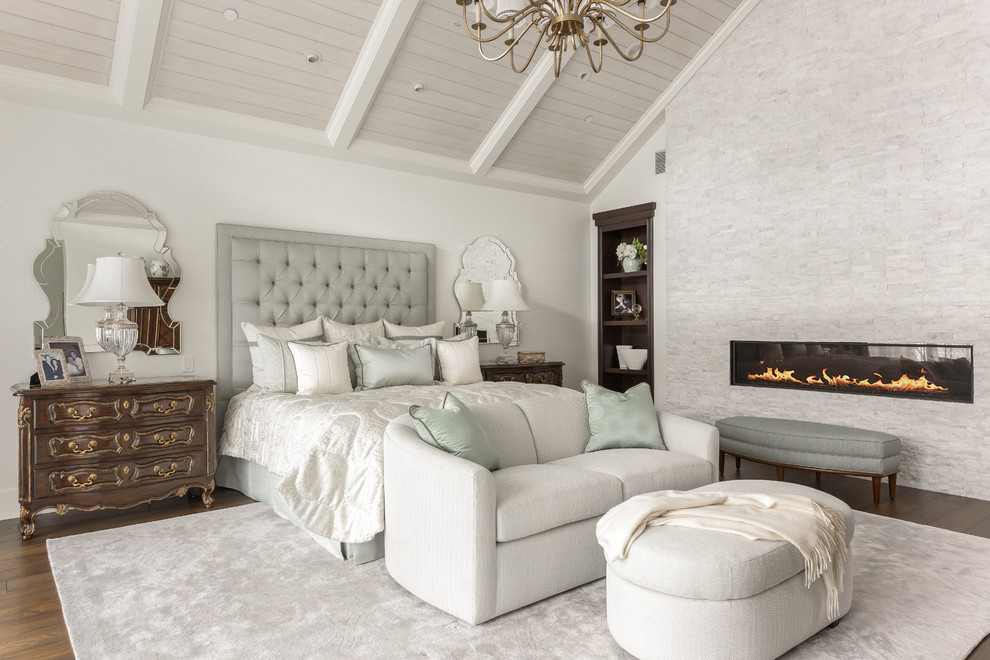 Photo of a large traditional master bedroom in Orange County with white walls, medium hardwood floors, a ribbon fireplace, a stone fireplace surround and brown floor.