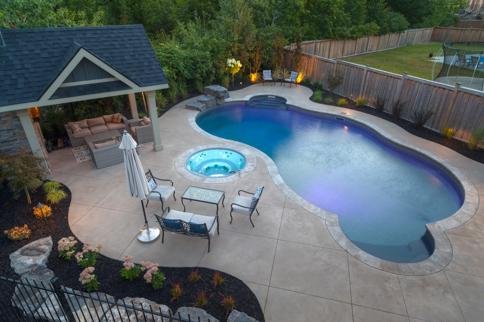 Large transitional backyard custom-shaped lap pool in Toronto with a hot tub and concrete pavers.