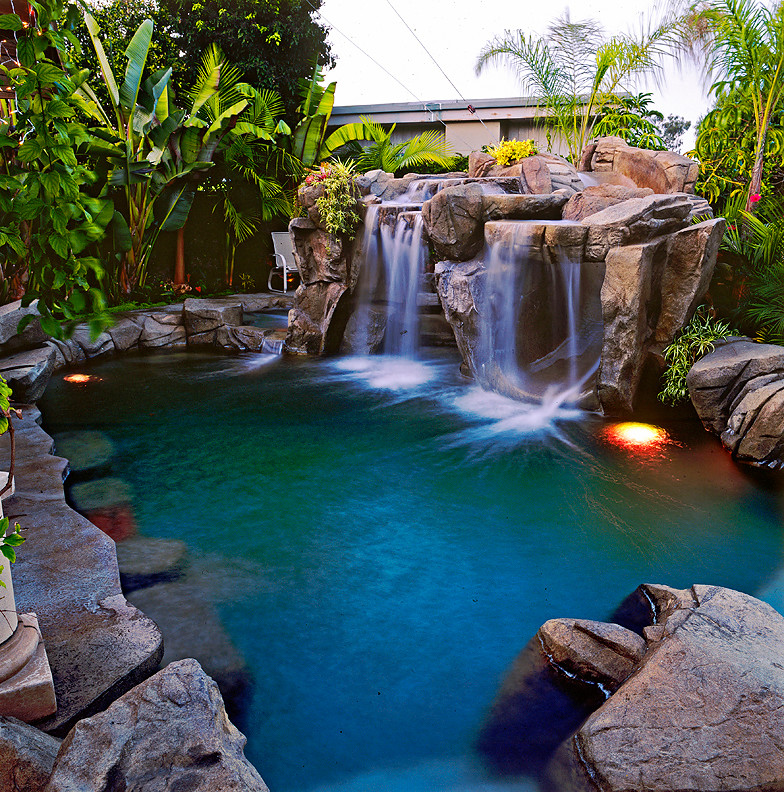 Photo of a tropical backyard custom-shaped pool in Orange County with a water slide and stamped concrete.