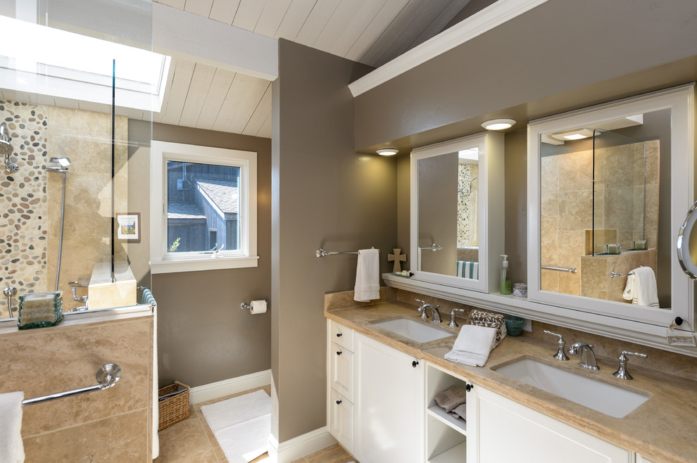 Photo of a mid-sized beach style master bathroom in San Francisco with shaker cabinets, white cabinets, a freestanding tub, a corner shower, a one-piece toilet, beige tile, pebble tile, grey walls, ceramic floors, an undermount sink, granite benchtops and beige floor.