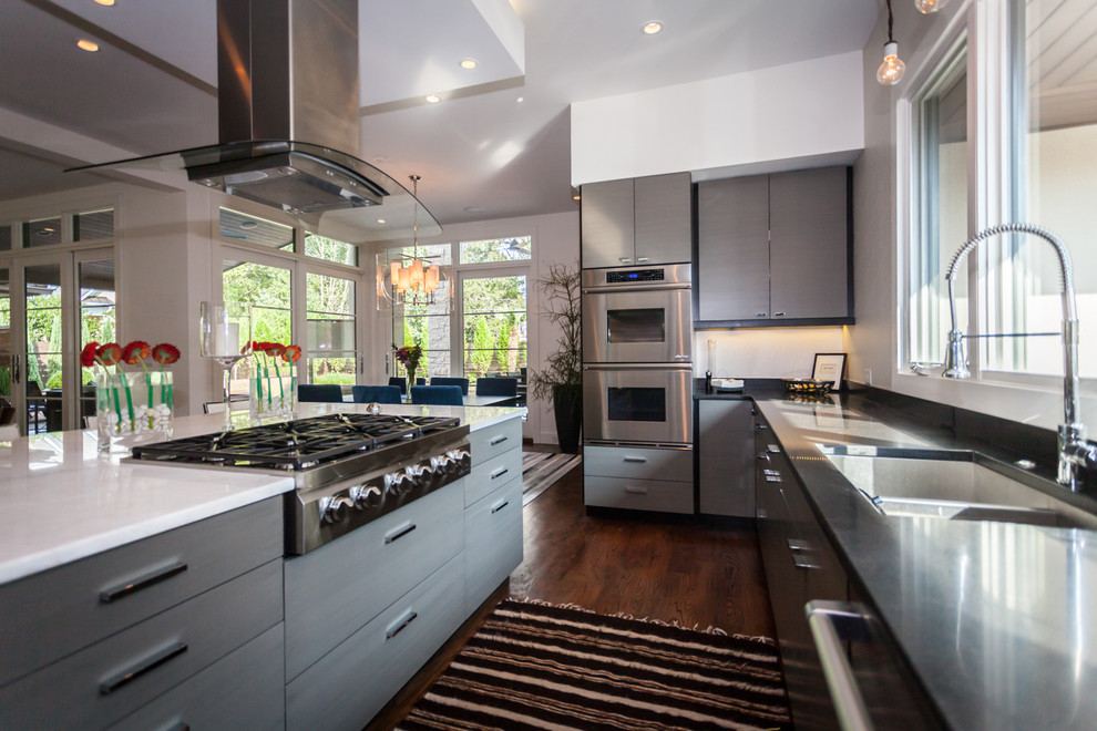 Photo of a large contemporary galley eat-in kitchen in Charlotte with a drop-in sink, flat-panel cabinets, grey cabinets, marble benchtops, black splashback, stone slab splashback, stainless steel appliances, medium hardwood floors and with island.