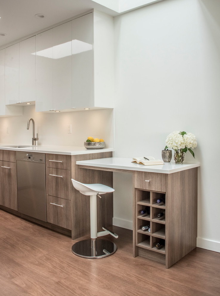This is an example of a beach style kitchen in Vancouver with an undermount sink, flat-panel cabinets, quartz benchtops, white splashback, stainless steel appliances, white benchtop, white cabinets and light hardwood floors.