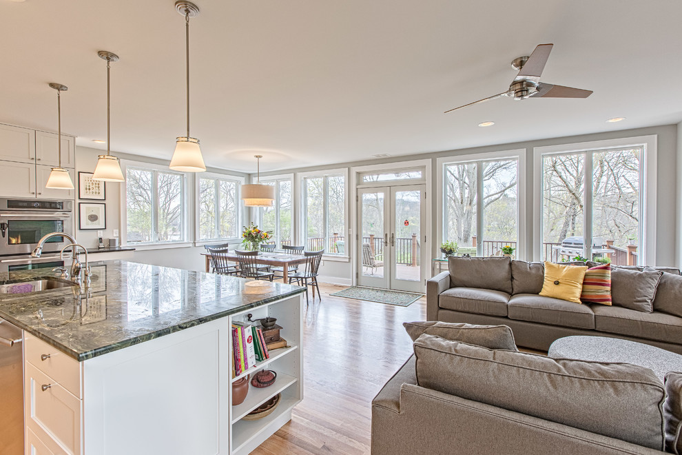 Example of a large transitional single-wall light wood floor open concept kitchen design in Detroit with an undermount sink, shaker cabinets, white cabinets, soapstone countertops, green backsplash, glass tile backsplash, stainless steel appliances and an island