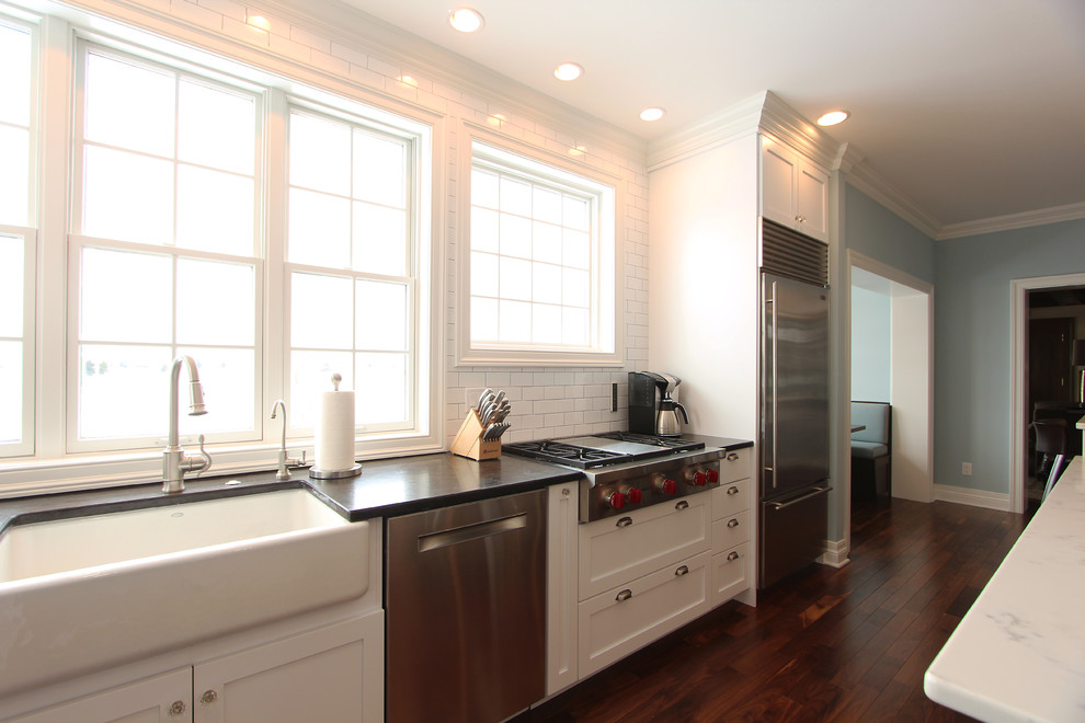 Inspiration for a large transitional u-shaped medium tone wood floor and brown floor eat-in kitchen remodel with a farmhouse sink, recessed-panel cabinets, white cabinets, quartz countertops, white backsplash, porcelain backsplash, stainless steel appliances and an island
