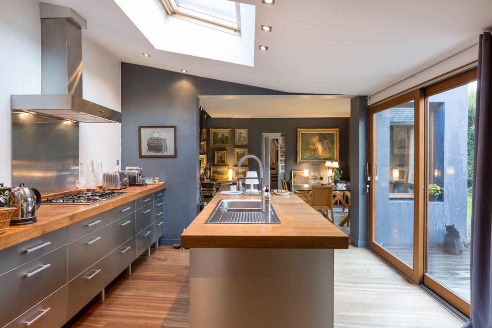 This is an example of a large contemporary galley open plan kitchen in Rennes with an undermount sink, stainless steel cabinets, wood benchtops, medium hardwood floors and with island.