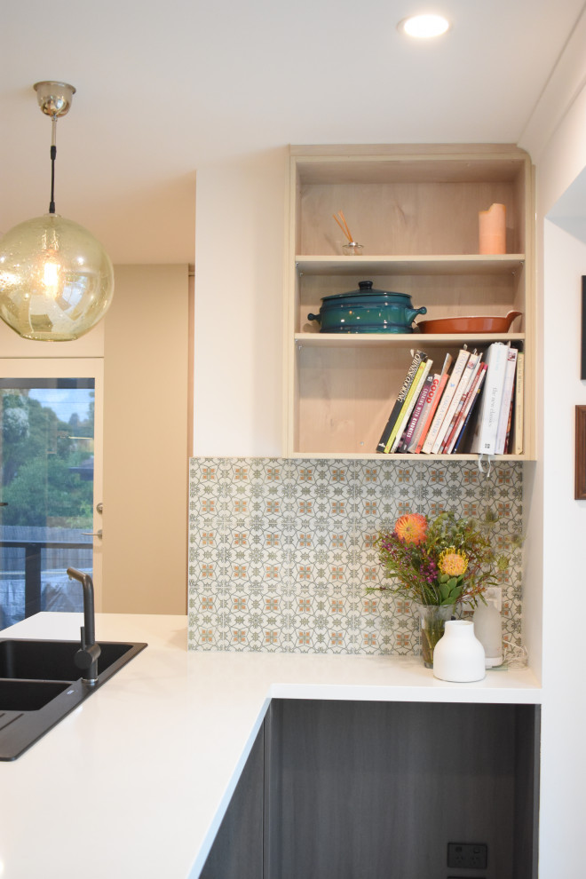 Mid-sized transitional galley eat-in kitchen in Melbourne with a double-bowl sink, flat-panel cabinets, green cabinets, quartz benchtops, grey splashback, mirror splashback, black appliances, laminate floors, a peninsula, brown floor and white benchtop.
