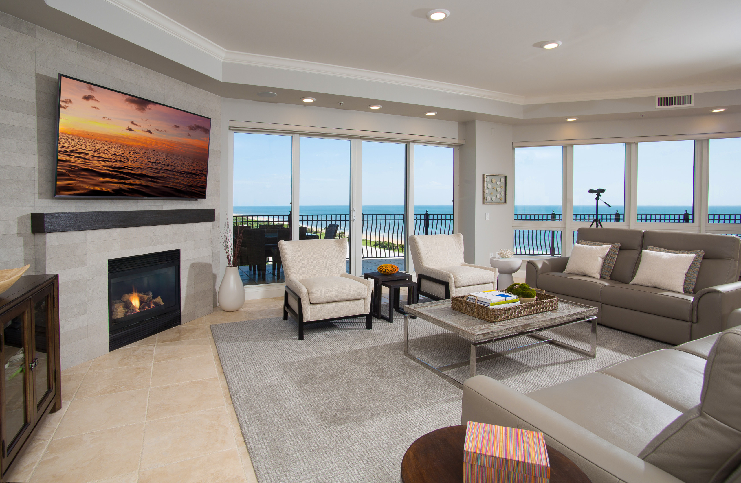 Example of a large beach style formal and open concept travertine floor and beige floor living room design in Orlando with beige walls, a standard fireplace, a stone fireplace and a wall-mounted tv
