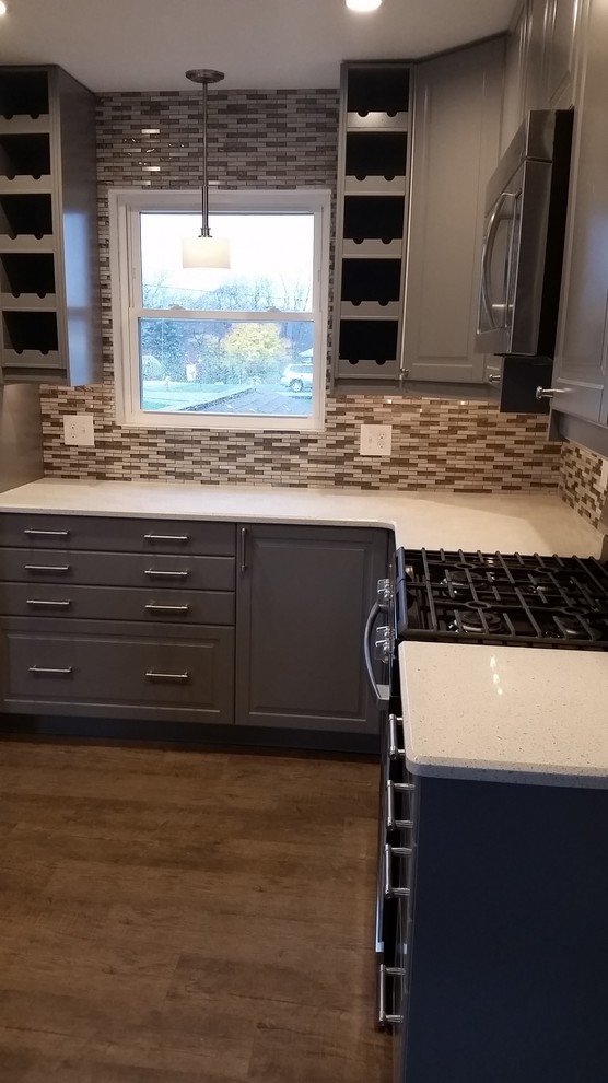 Photo of a small transitional l-shaped eat-in kitchen in Other with a farmhouse sink, raised-panel cabinets, grey cabinets, quartz benchtops, grey splashback, metal splashback, stainless steel appliances, vinyl floors and with island.