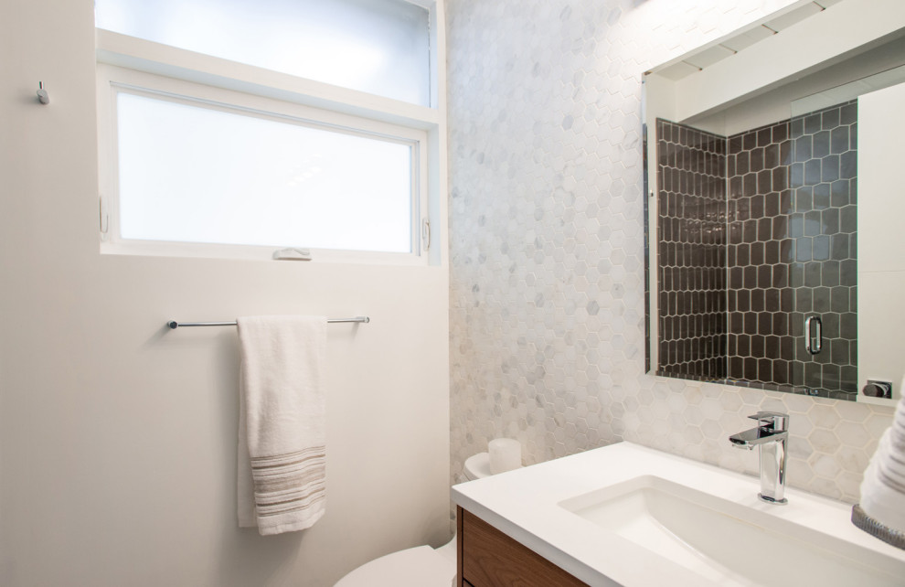 Mid-sized trendy master white tile and subway tile mosaic tile floor and multicolored floor bathroom photo in Other with flat-panel cabinets, medium tone wood cabinets, a one-piece toilet, white walls, an undermount sink, quartz countertops, a hinged shower door and white countertops
