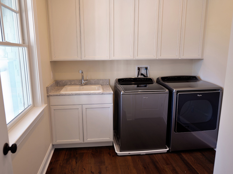 This is an example of a mid-sized beach style single-wall dedicated laundry room in Other with a drop-in sink, recessed-panel cabinets, white cabinets, granite benchtops, medium hardwood floors, a side-by-side washer and dryer and beige walls.