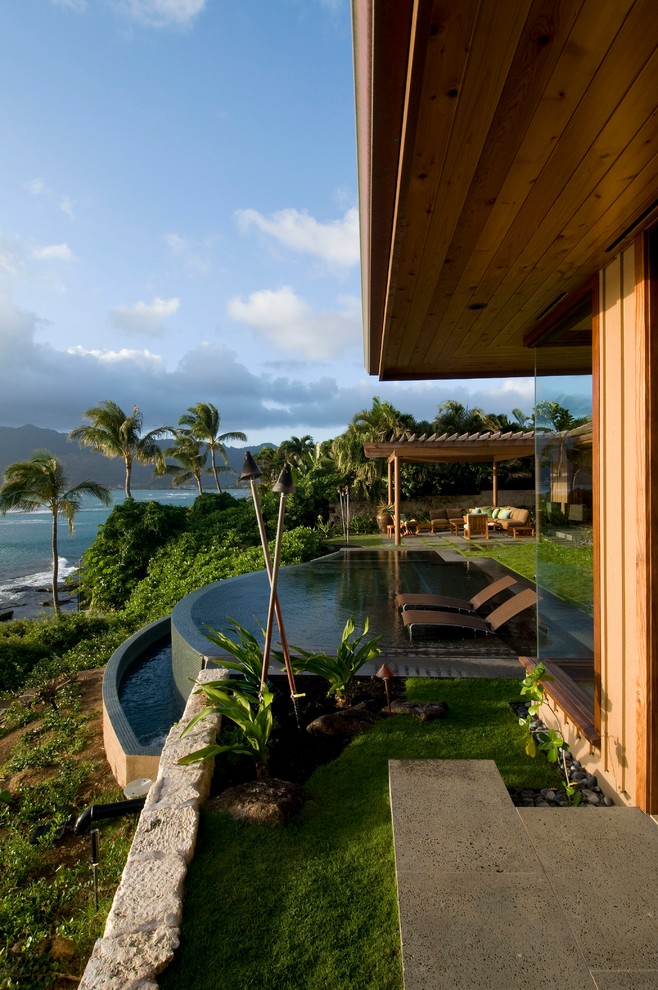 Inspiration for a large tropical backyard round infinity pool in Hawaii with concrete pavers.