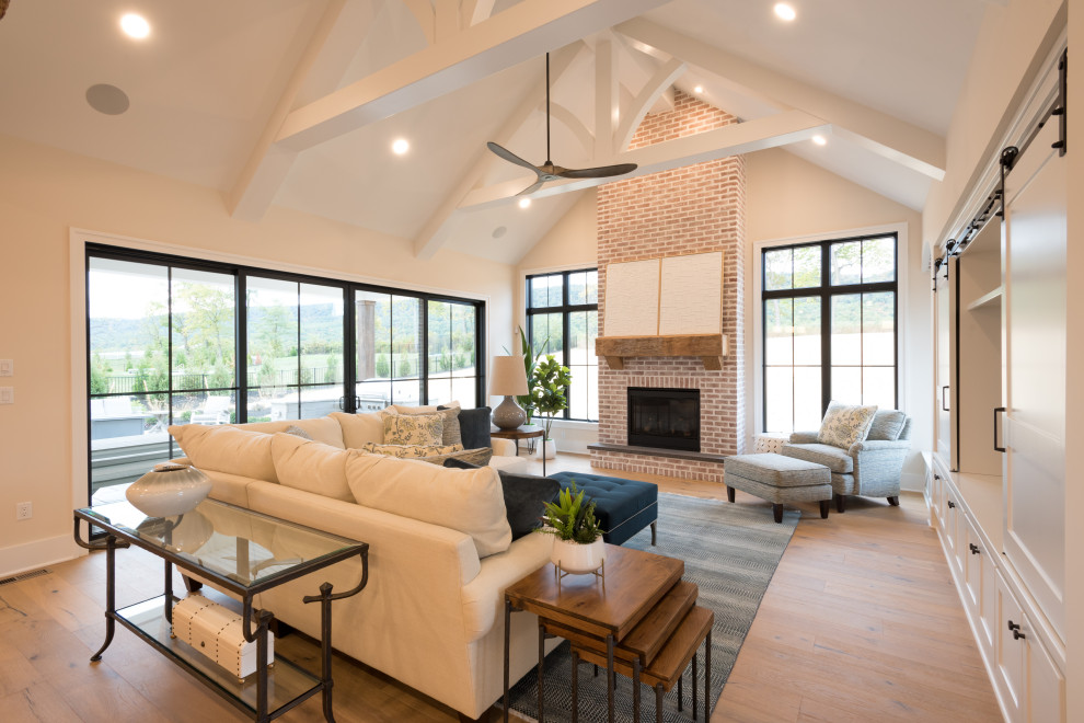 This is an example of an expansive country open concept living room in Other with white walls, medium hardwood floors, a standard fireplace, a brick fireplace surround, a built-in media wall, brown floor and vaulted.