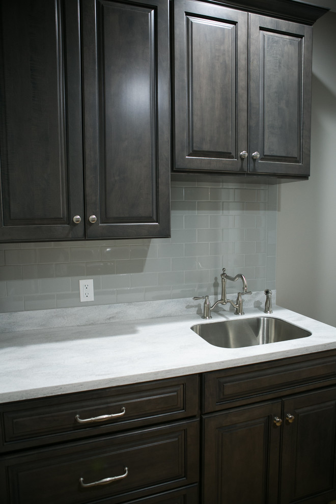 Photo of a small transitional galley dedicated laundry room in Indianapolis with an undermount sink, raised-panel cabinets, dark wood cabinets, grey walls, medium hardwood floors, a side-by-side washer and dryer, brown floor and white benchtop.