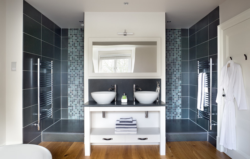 Inspiration for a contemporary bathroom in London with a vessel sink, open cabinets, white cabinets, an alcove shower, gray tile, mosaic tile, white walls and medium hardwood floors.
