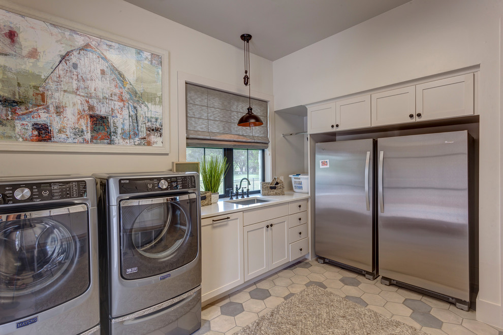 Photo of a mid-sized country l-shaped utility room in Austin with an undermount sink, shaker cabinets, white cabinets, quartz benchtops, white walls, ceramic floors, a side-by-side washer and dryer, beige floor and white benchtop.