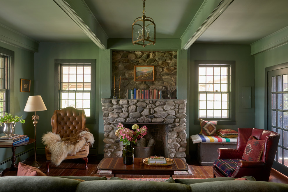 Country family room in New York with green walls, no tv, medium hardwood floors, a standard fireplace, a stone fireplace surround and exposed beam.