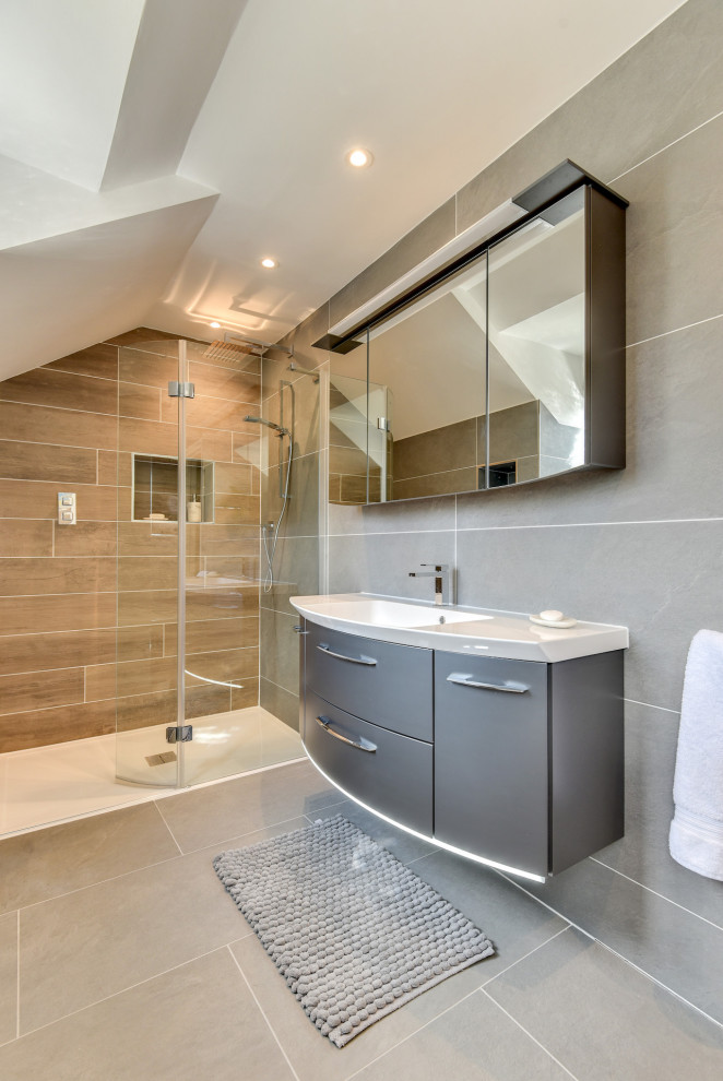 Large modern grey and white ensuite bathroom in Sussex with flat-panel cabinets, grey cabinets, a freestanding bath, a walk-in shower, a one-piece toilet, grey tiles, ceramic tiles, grey walls, ceramic flooring, a built-in sink, glass worktops, grey floors, an open shower, white worktops, feature lighting, a single sink and a floating vanity unit.