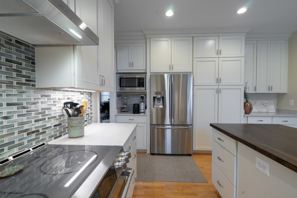 Photo of a traditional u-shaped eat-in kitchen in DC Metro with an undermount sink, flat-panel cabinets, white cabinets, quartzite benchtops, multi-coloured splashback, ceramic splashback, stainless steel appliances, light hardwood floors, with island, yellow floor and white benchtop.