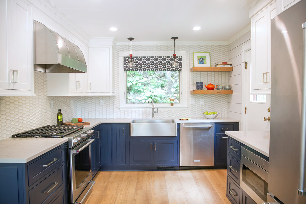 Small beach style u-shaped separate kitchen in Milwaukee with a farmhouse sink, recessed-panel cabinets, blue cabinets, quartz benchtops, white splashback, porcelain splashback, stainless steel appliances, light hardwood floors, beige benchtop and beige floor.